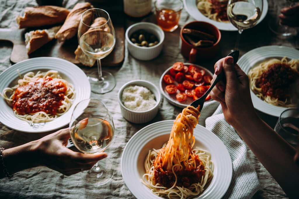 Mesa italiana com pratos de espaguete ao molho de tomate, vinho e acompanhamentos.