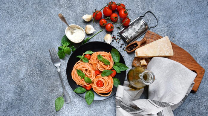 Prato de espaguete com molho de tomate e manjericão, cercado por ingredientes italianos frescos.