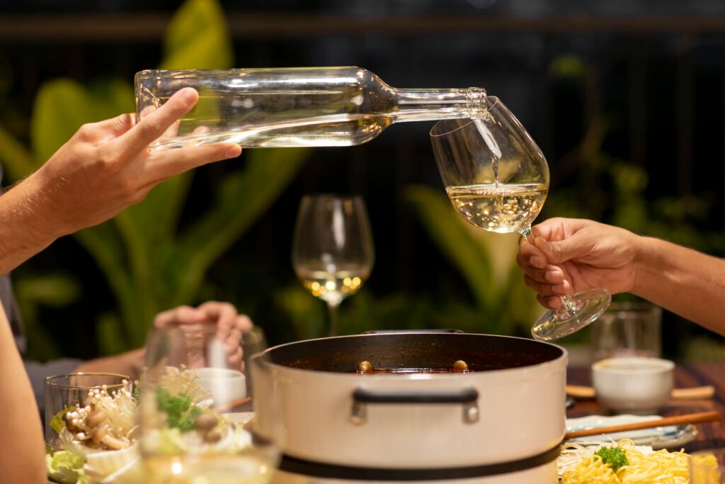 Servindo vinho branco em taça durante refeição com pratos variados à mesa.