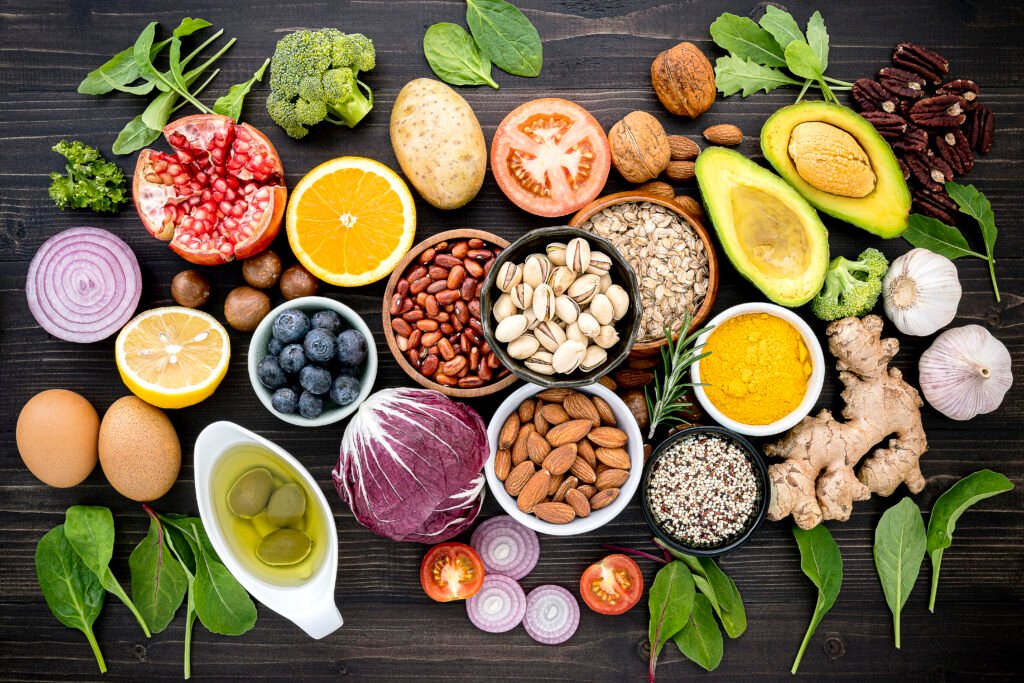 Superfoods organizadas em uma mesa de madeira escura, incluindo frutas, vegetais, sementes, nozes e especiarias.