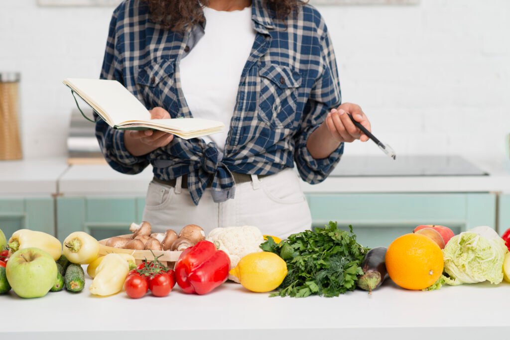 Pessoa planejando receitas funcionais com um caderno de anotações e ingredientes frescos em uma cozinha.