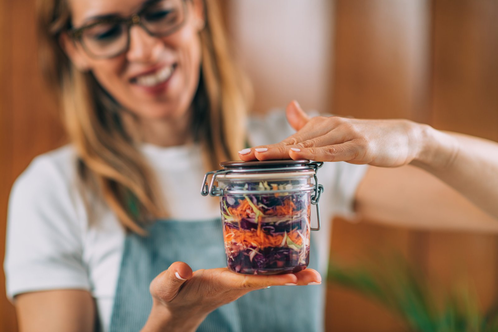 Mulher segurando um pote de vidro com salada colorida, mostrando uma receita prática de um-pote.