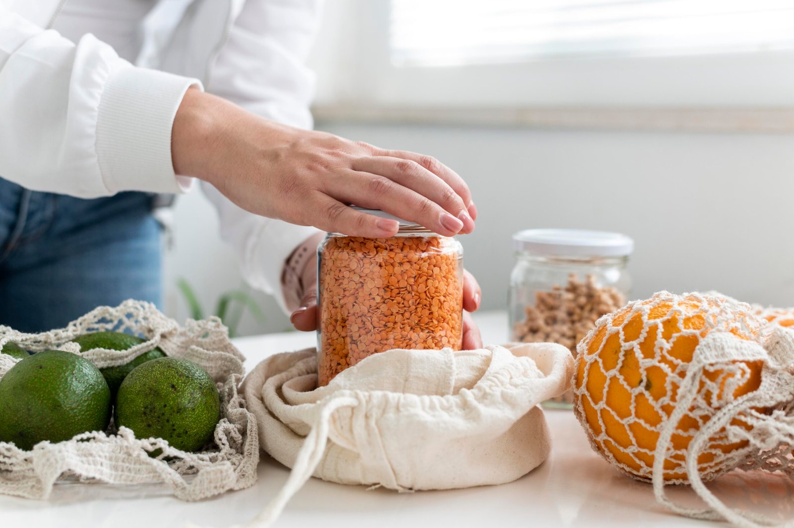 Pessoa armazenando lentilhas em um pote de vidro com alimentos em sacolas reutilizáveis ao redor.