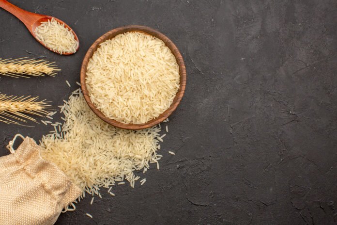 Grãos de arroz integral em tigela de madeira com fundo rústico escuro.