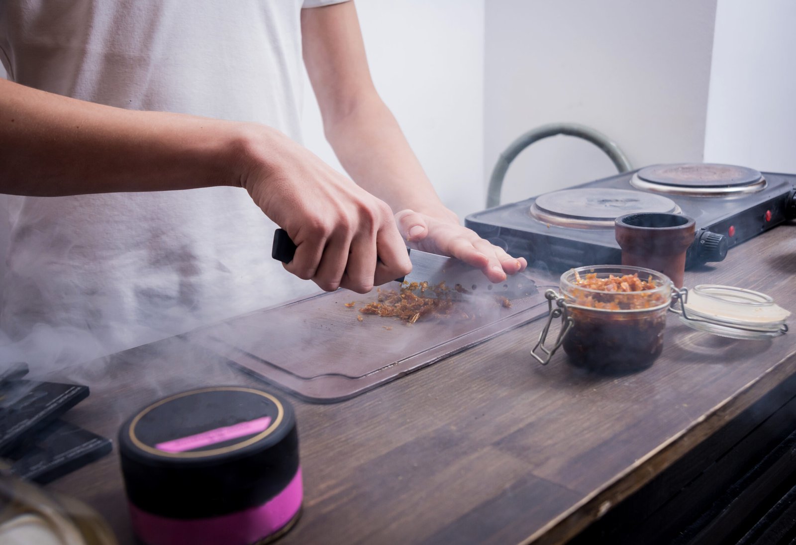 Pessoa cortando alimentos enquanto realiza defumação caseira em um ambiente simples.