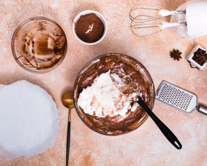 Mistura de mousse de chocolate em uma tigela, com utensílios e ingredientes para confeitaria.