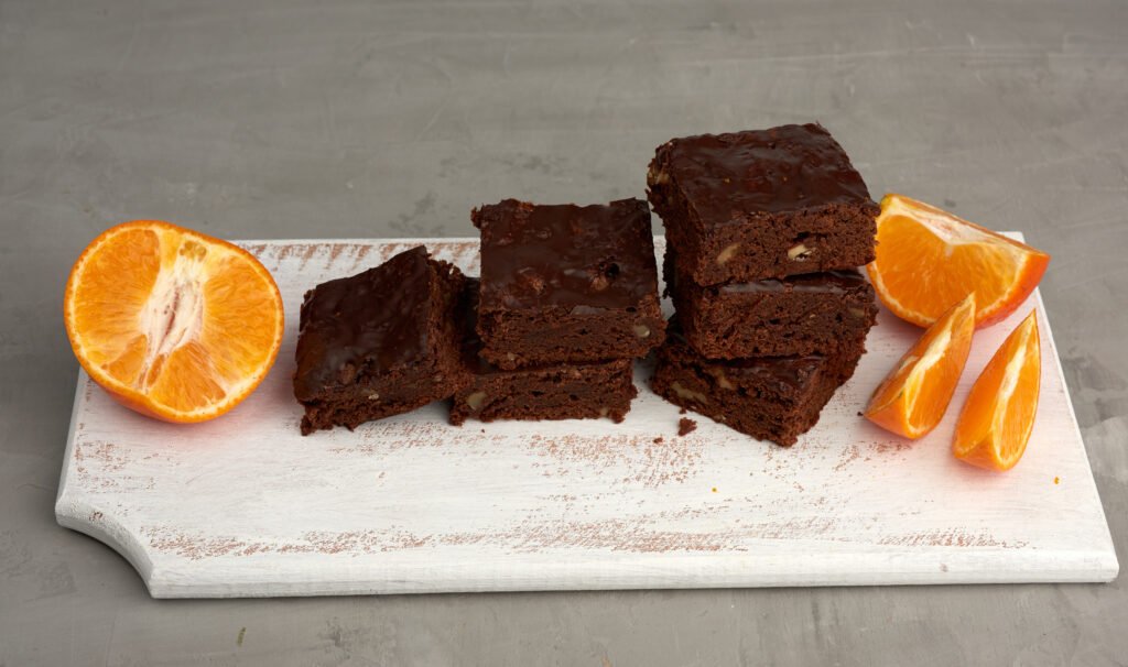 Brownie de café com toque de laranja servido com fatias de laranja fresca em uma tábua branca.