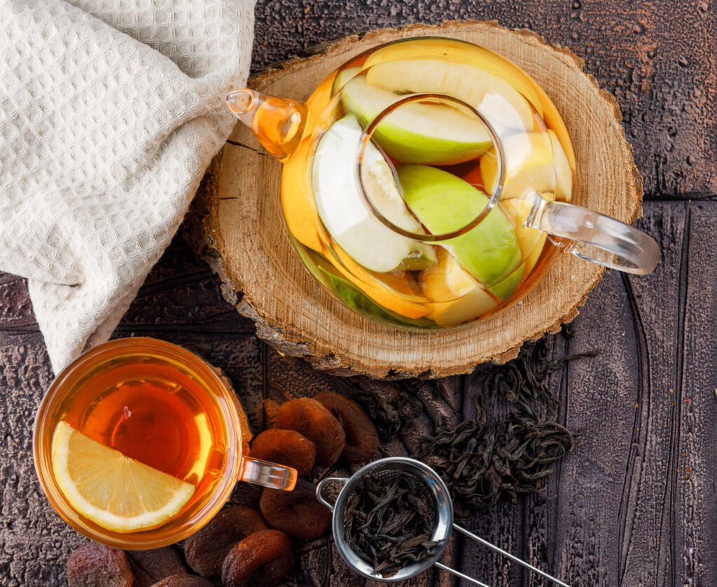 Jarra de infusão de frutas com fatias de maçã e chá, sobre uma base de madeira.