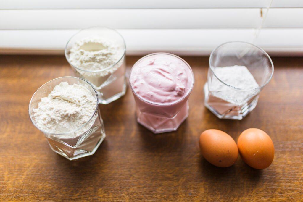 Ingredientes para espumas culinárias, incluindo ovos, farinha e creme em recipientes de vidro sobre uma mesa de madeira.