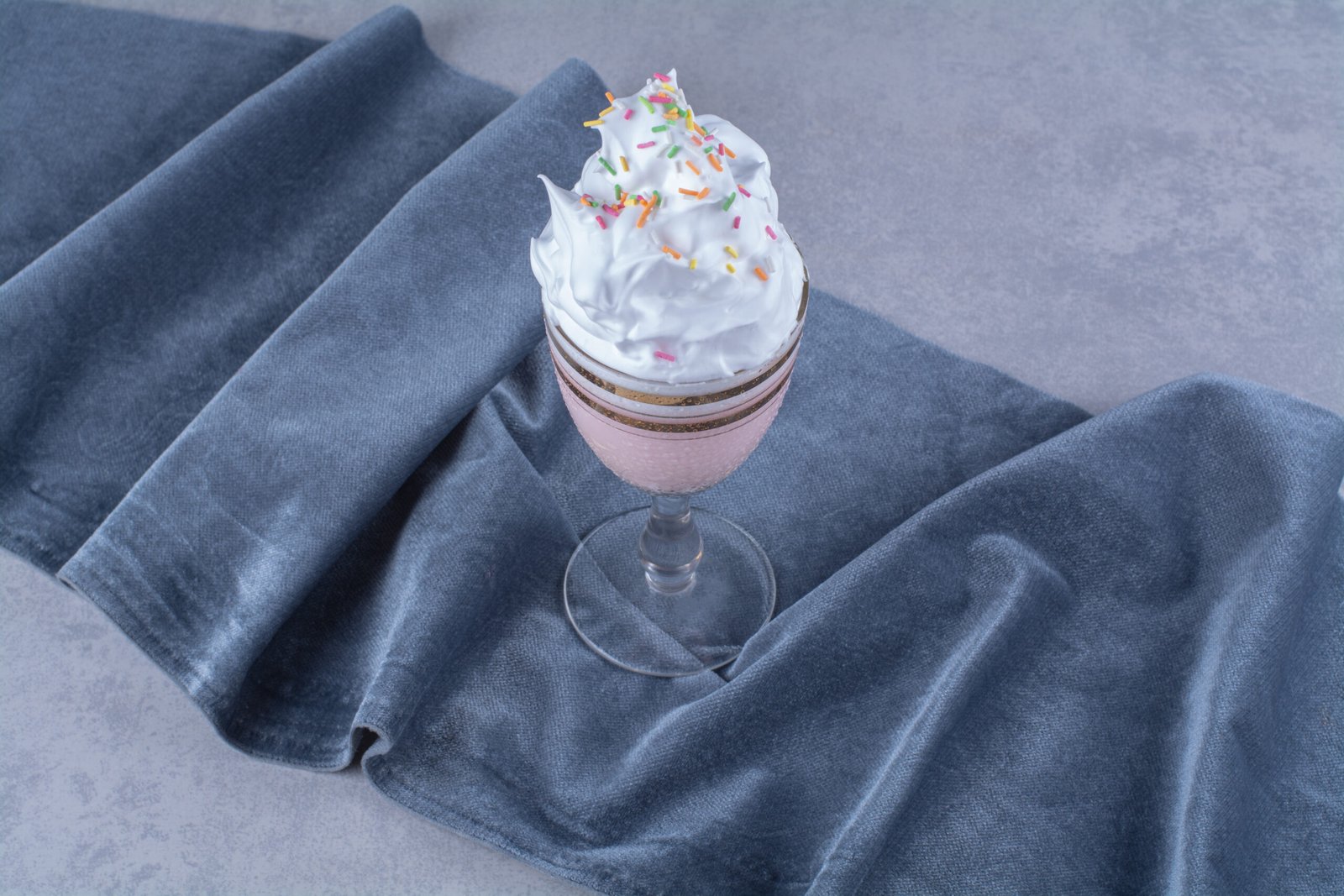 Taça com sobremesa de espuma doce decorada com confeitos coloridos sobre um tecido azul.