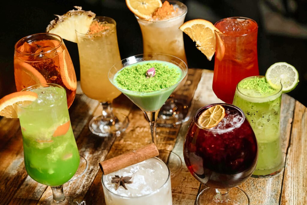 Mocktails criativos variados decorados com frutas cítricas e ervas frescas, servidos em diferentes copos sobre uma mesa de madeira.