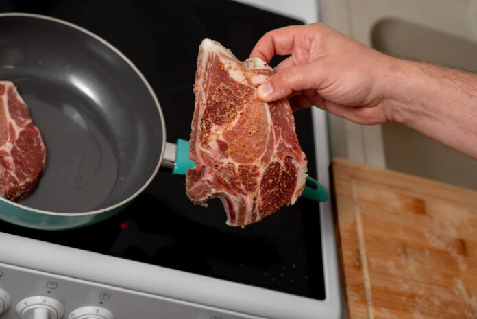 Mão colocando um pedaço de carne temperada em uma frigideira quente.