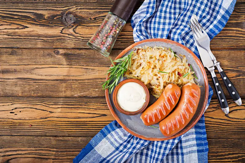 Prato clássico da cozinha alemã com salsichas grelhadas, chucrute e molho cremoso, acompanhado de um ramo de alecrim.