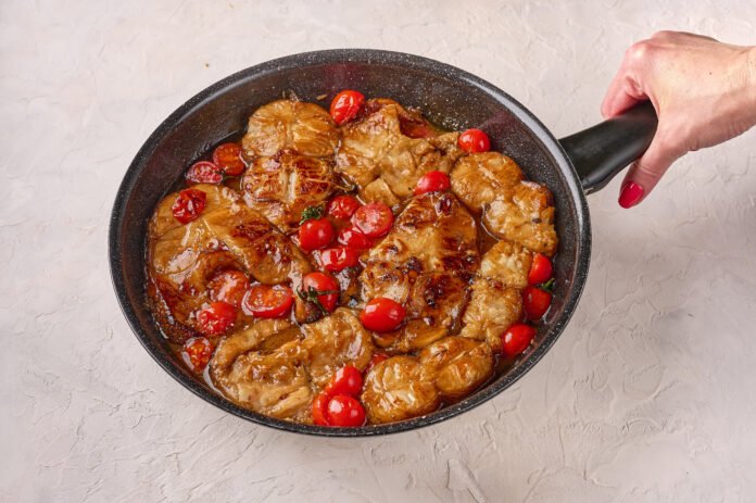 Frigideira com pedaços de carne suculenta e tomates cereja em molho caramelizado.