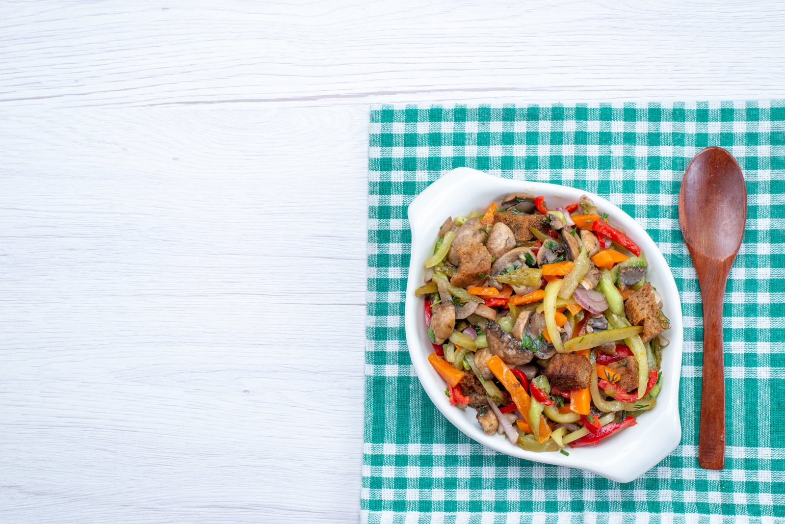 Salada colorida feita com cascas de legumes variados em uma tigela branca sobre uma toalha xadrez verde.