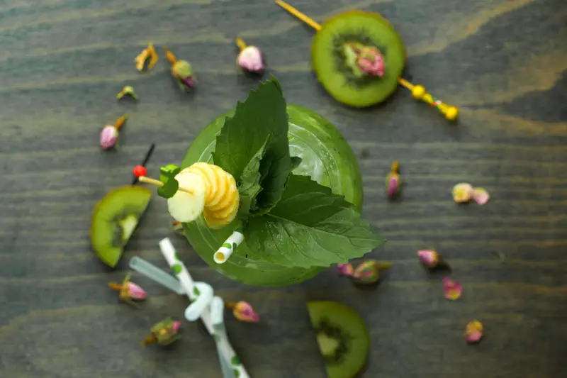 Drink tropical com ervas frescas, kiwi e decoração elegante em um fundo de madeira.