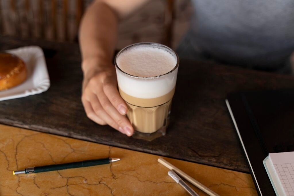 Copo de latte artesanal com espuma cremosa em uma mesa de madeira, acompanhado de itens de escritório.