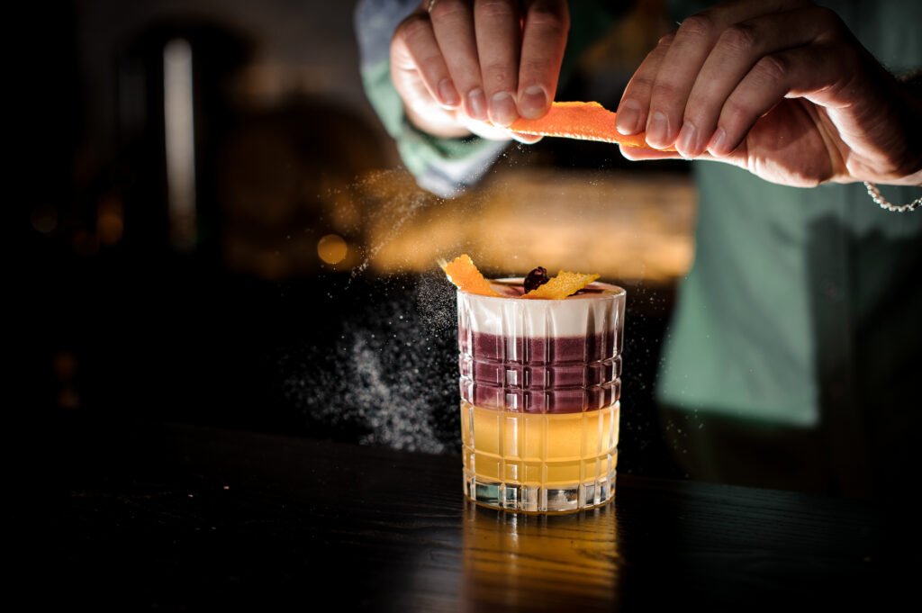 Bartender preparando um coquetel sofisticado com raspas de laranja para harmonizar com sobremesas.