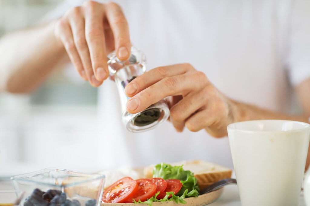 Pessoa usando um moedor para temperar uma salada com tomate e alface, destacando a moderação no uso de sal.