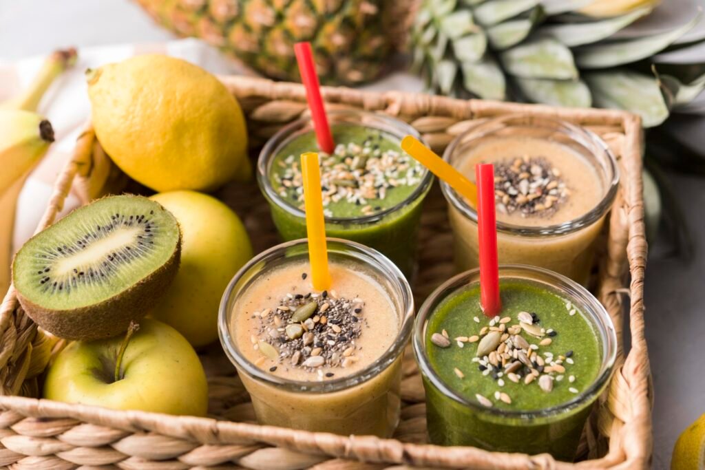 Smoothies com superfoods em cesta de palha, acompanhados por frutas frescas como kiwi, maçã e limão.