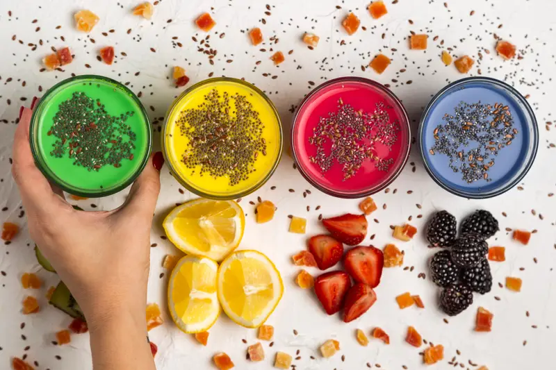 Smoothies coloridos com superfoods e frutas frescas em fundo branco.